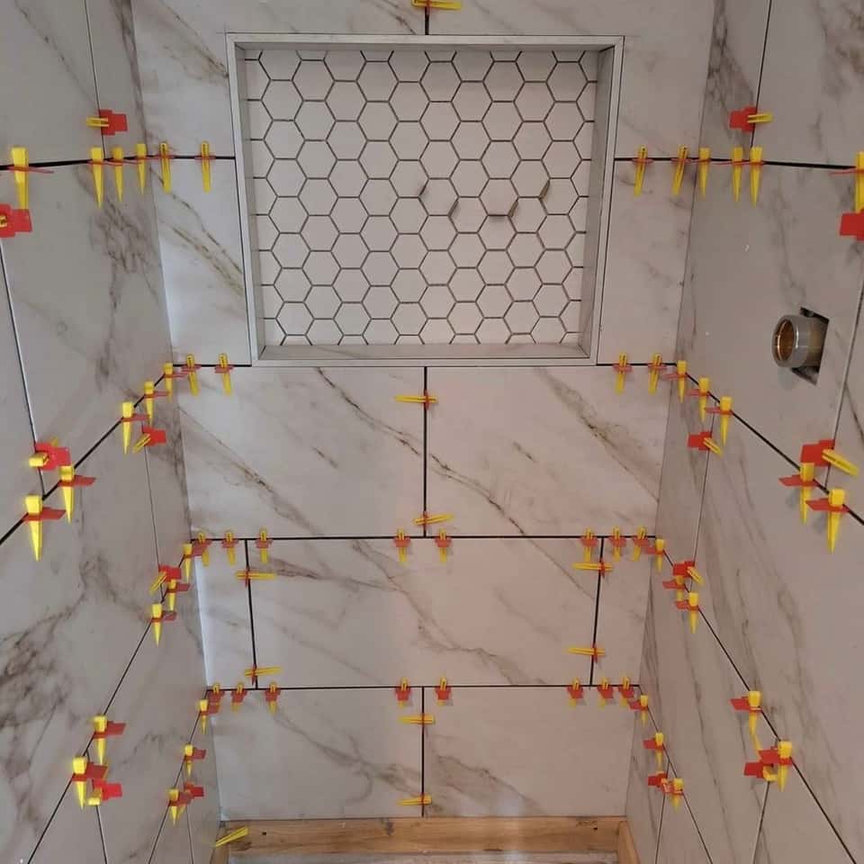 Tile shower wall mid-set with levelling clips around a mosaic niche — Cristian House Remodeling LLC